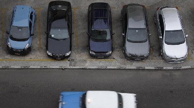 A vintage automobile drives by a parking lot of modern vehicles in Havana, Cuba